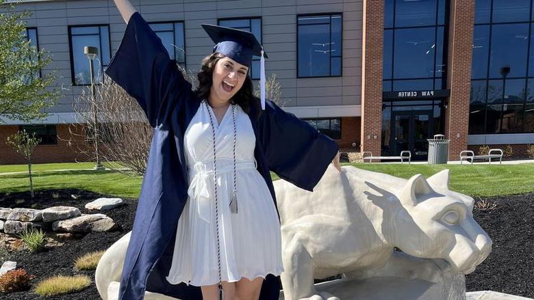 New Penn State graduate Anna Raffeinner celebrates with a joyful expression with the Lion Shrine on the Penn State 杜波依斯 campus, 就在PAW中心外面